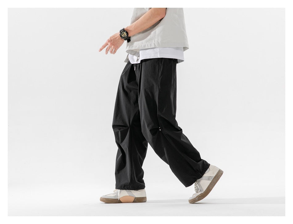 Cropped model walking in loose black trousers with a drawstring waist and gathered hems, shown from the side.