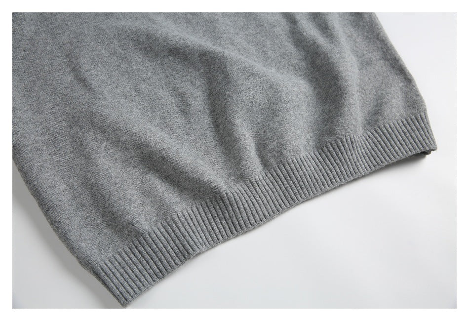 Close-up of a heather gray knit garment with a wide ribbed hem laid on a white surface.