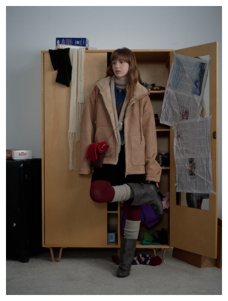 Model wearing a tan shearling-lined jacket with layered knitwear, a black skirt, burgundy tights and tall boots.
