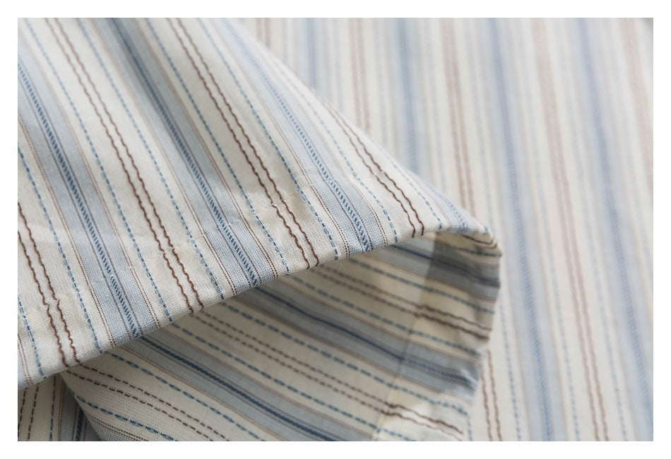 Close-up of draped cream fabric with fine blue and brown stripes.