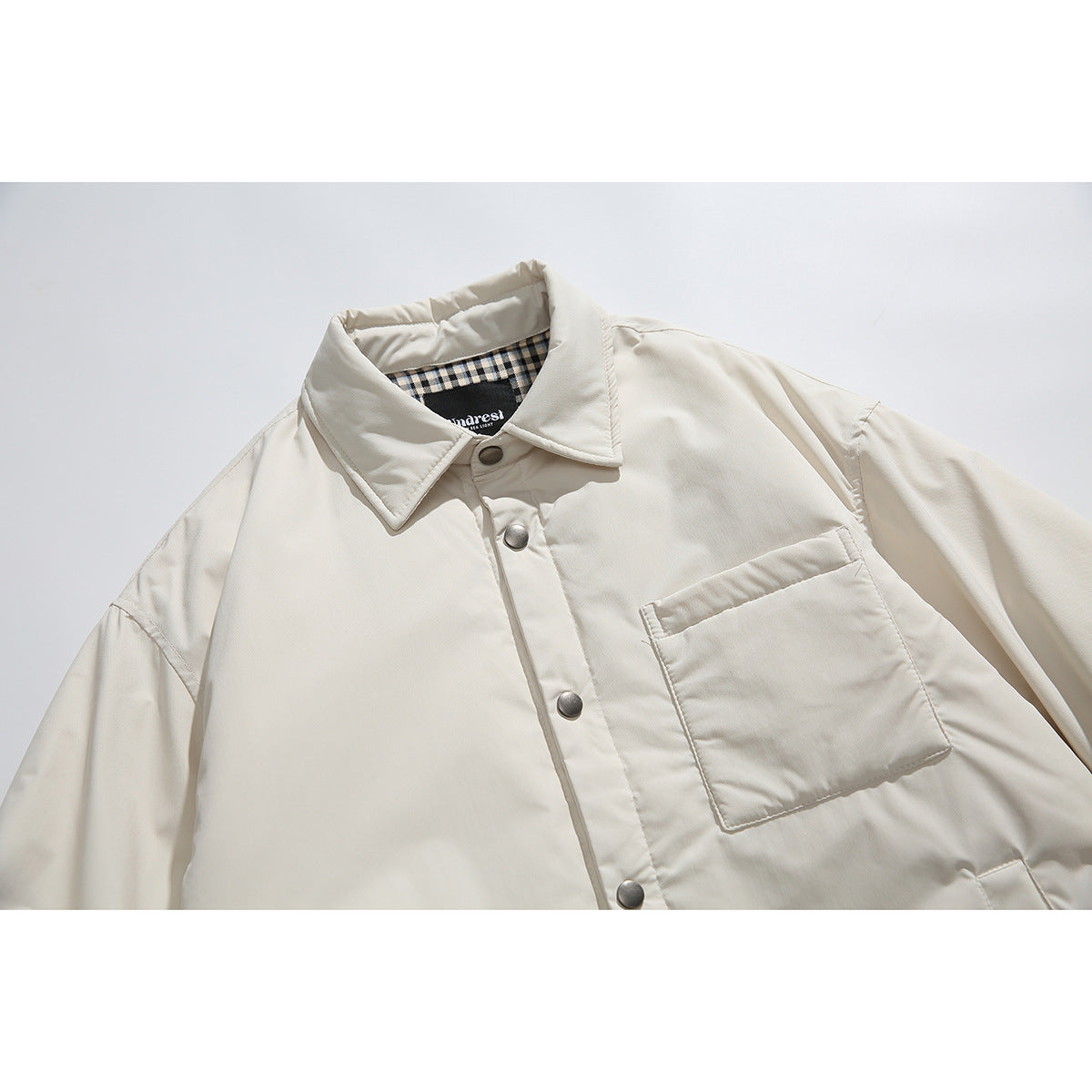 Close-up of an ivory shirt jacket front with snap buttons, a chest pocket and checked collar lining.