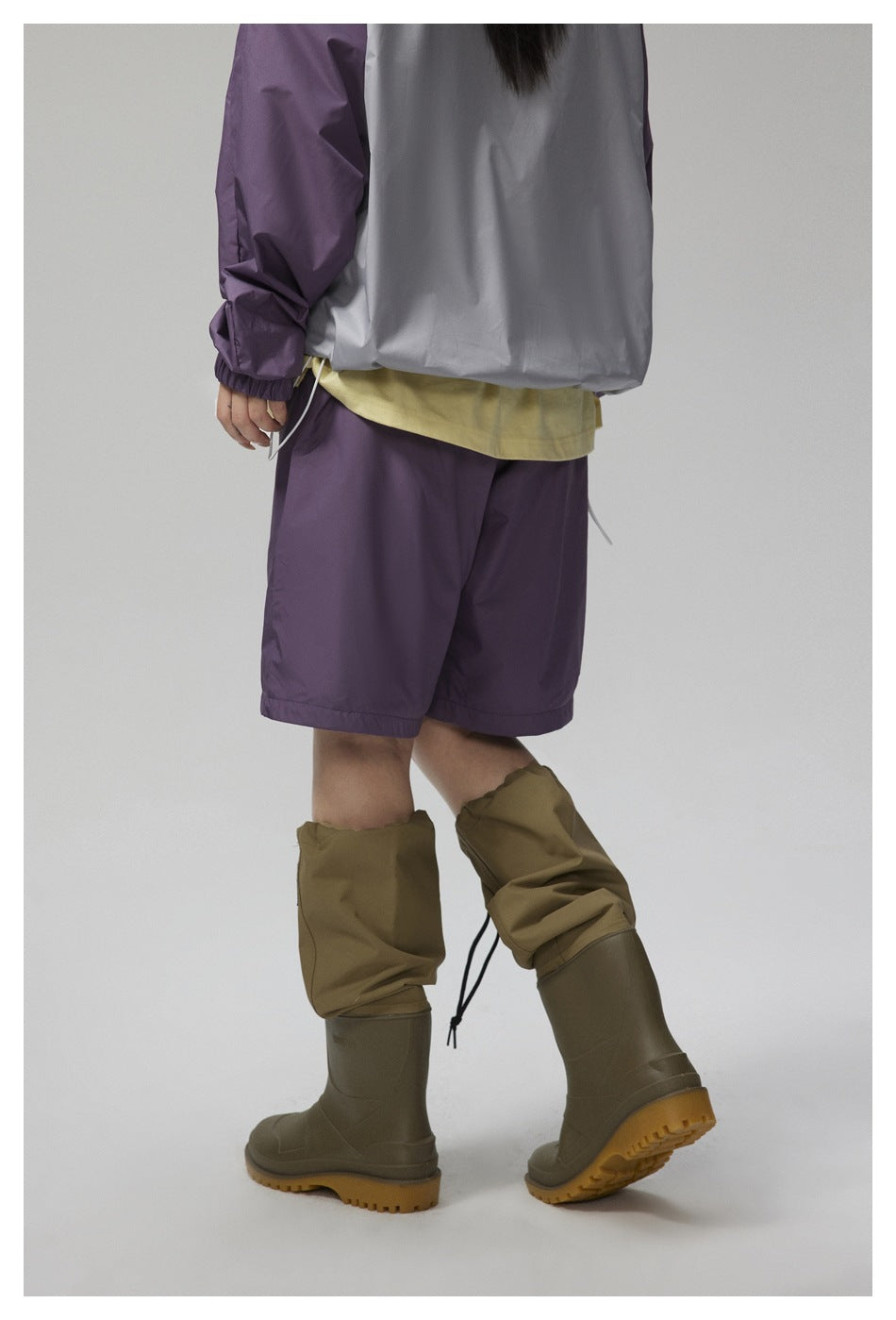 Rear view of a model wearing purple shorts and olive rain boots with adjustable gaiter covers.