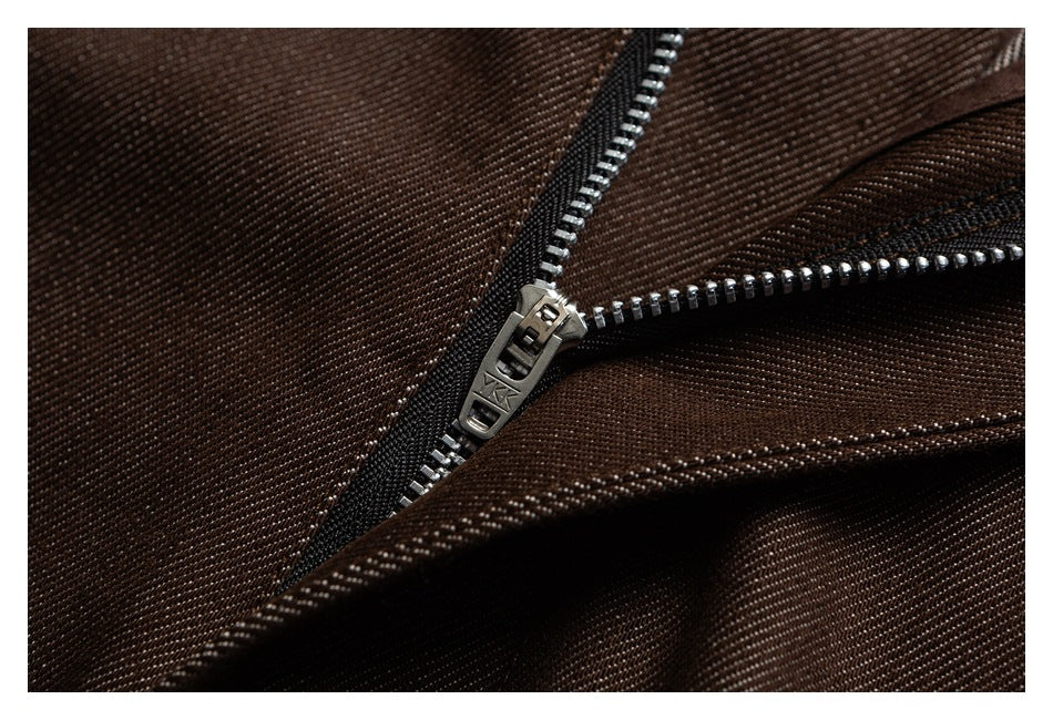 Close-up of a metal zipper and stitching on dark brown trousers.