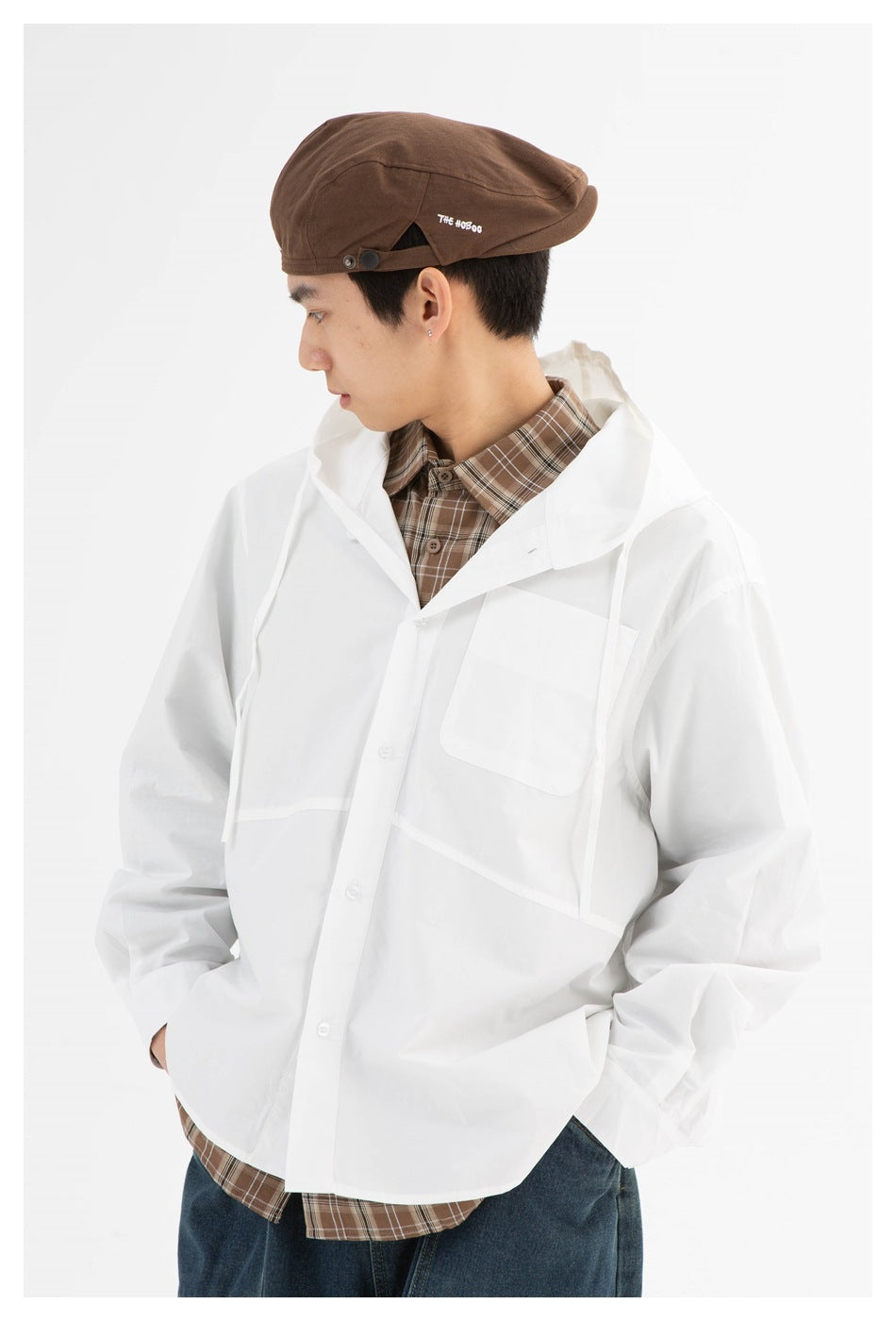 Close view of a model wearing a white hooded jacket with a chest pocket over a brown plaid shirt.