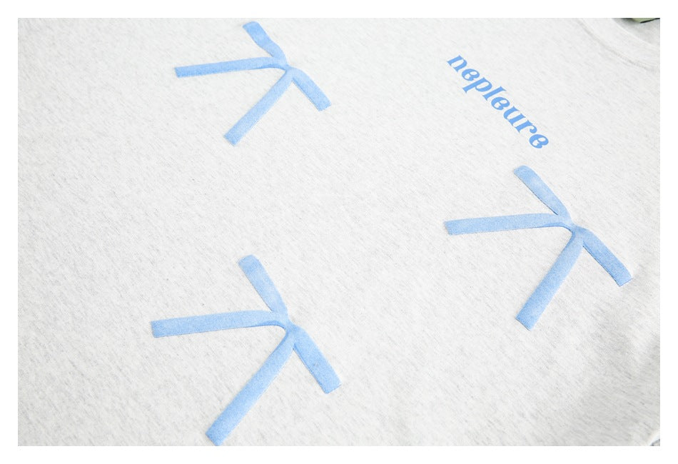 Close-up of a light gray garment with blue bow motifs and NEPLEURE lettering.