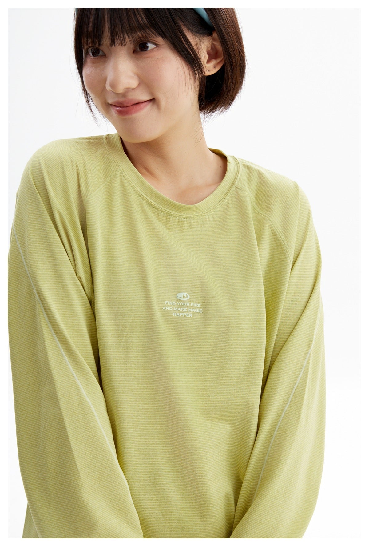 Close-up of a woman wearing a pale yellow-green fine-striped long-sleeve shirt with a small white chest print.