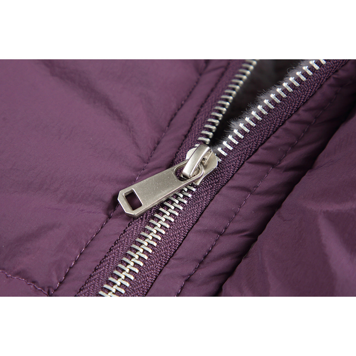 Close-up of a silver zipper and pull on plum padded jacket fabric.