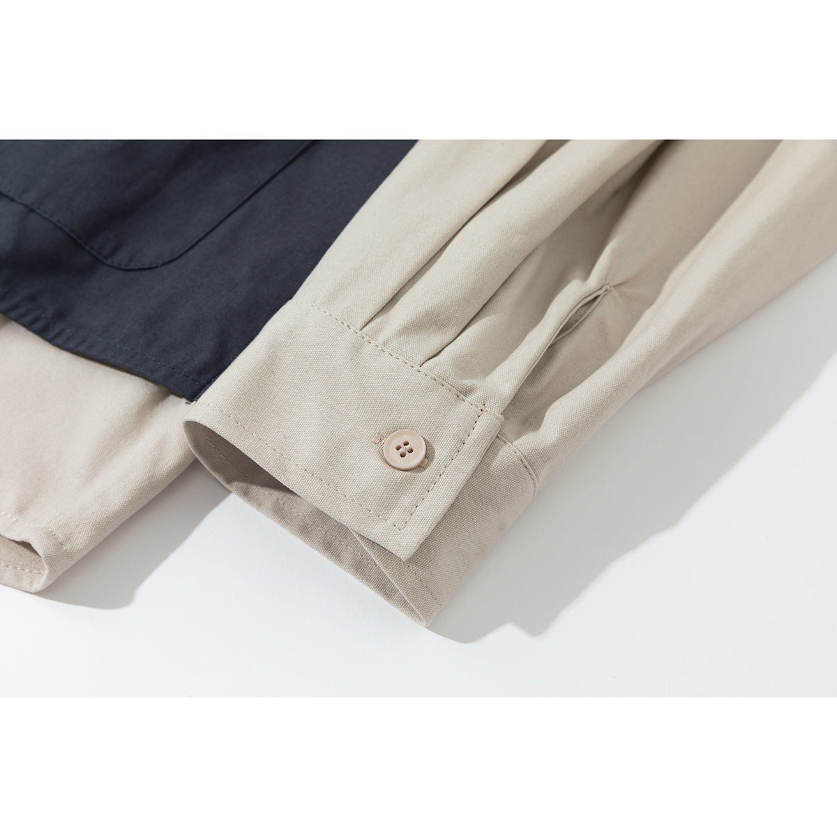 Close-up of a cream shirt cuff with a light button, beside part of a navy garment.