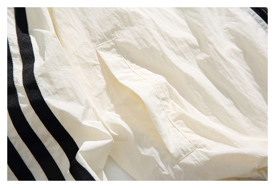 Close-up of a stitched pocket on crinkled ivory fabric beside wide black stripe trim.
