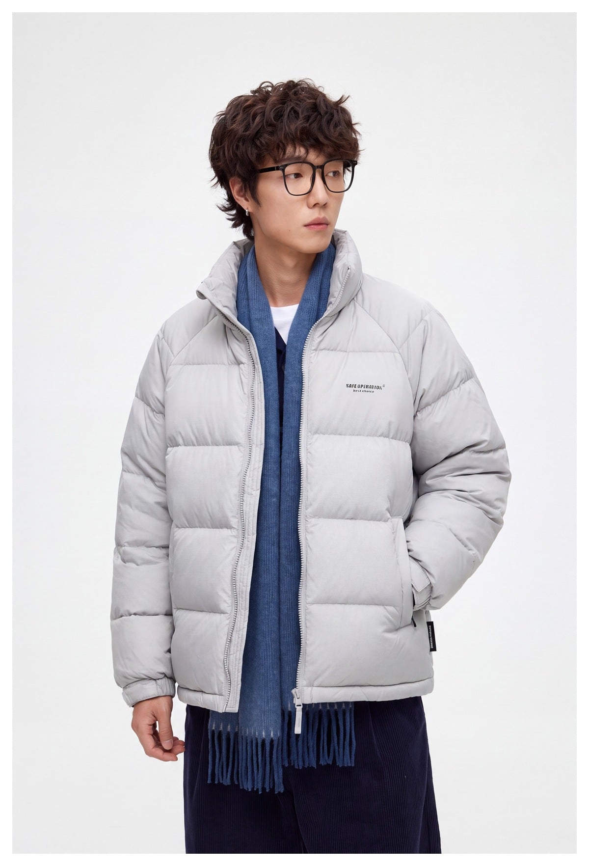 Model wearing a light gray quilted puffer jacket with a high collar, styled with a blue scarf and dark trousers.