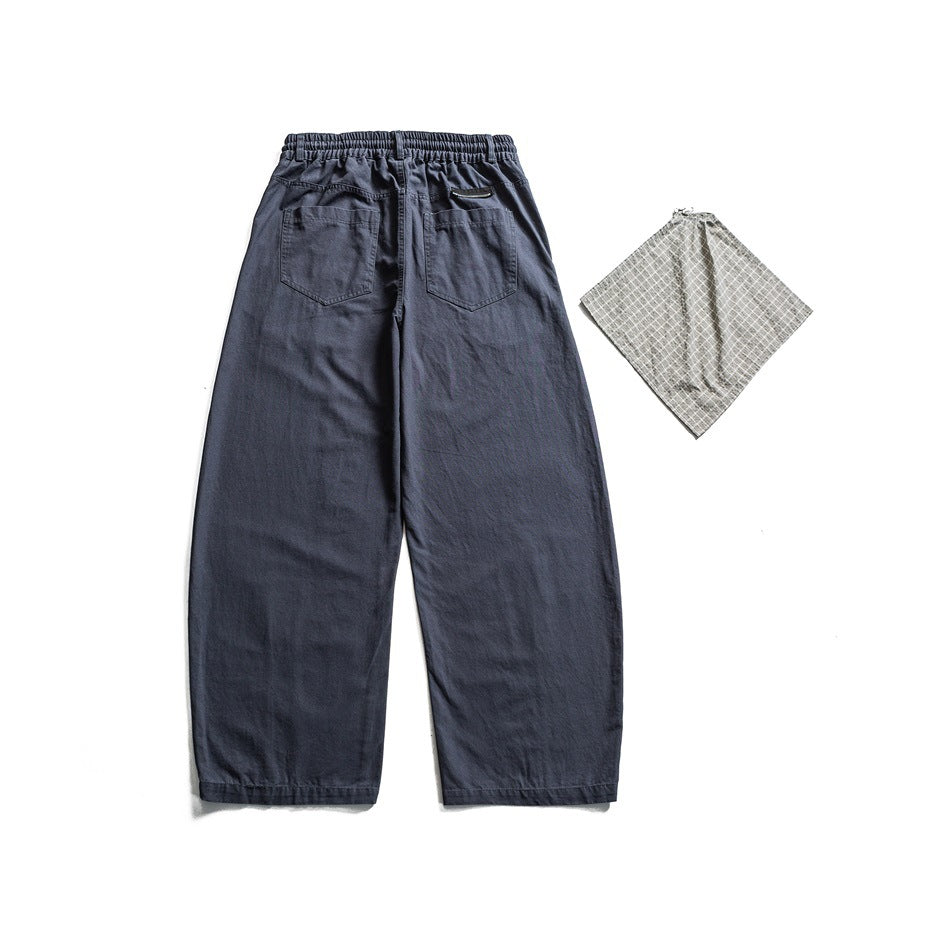Back view of slate blue wide-leg trousers with an elastic waist, two rear pockets, and a patterned fabric swatch beside them.
