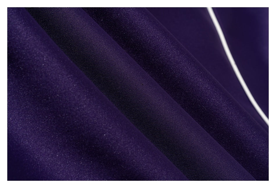 Extreme close-up of dark purple garment fabric, a smooth diagonal panel, and narrow white piping.