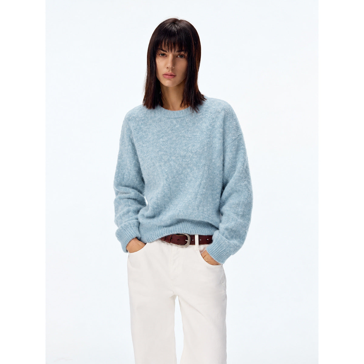 Model wearing a light blue crew-neck sweater with ribbed cuffs and hem, paired with white trousers.