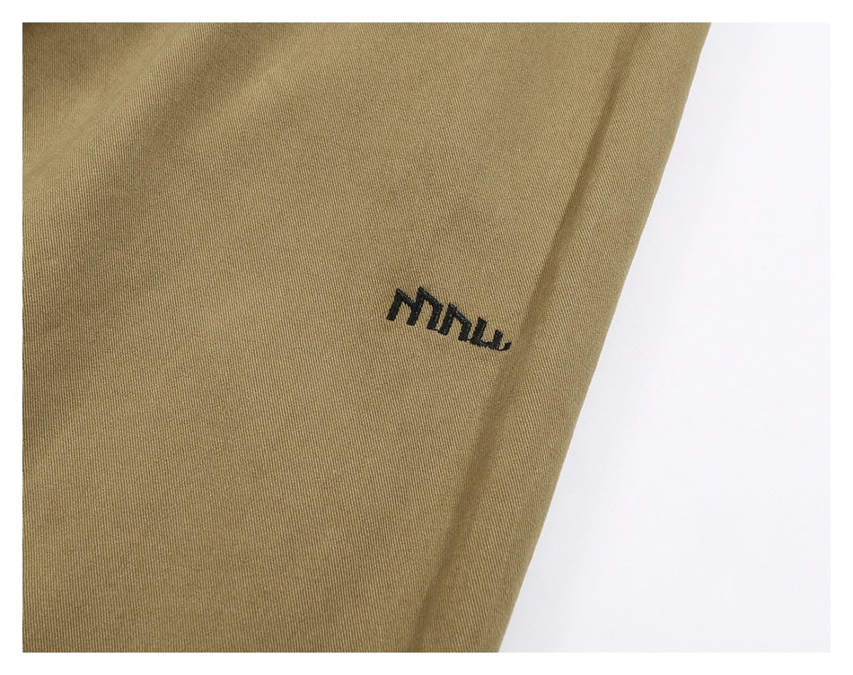 Close-up of khaki trouser fabric with a small black embroidered mark.