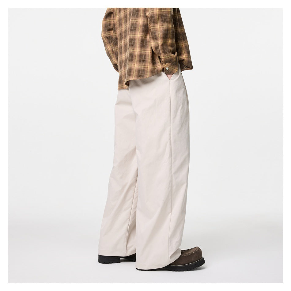 Side view of a model wearing ivory wide-leg trousers with a brown plaid shirt and dark shoes.