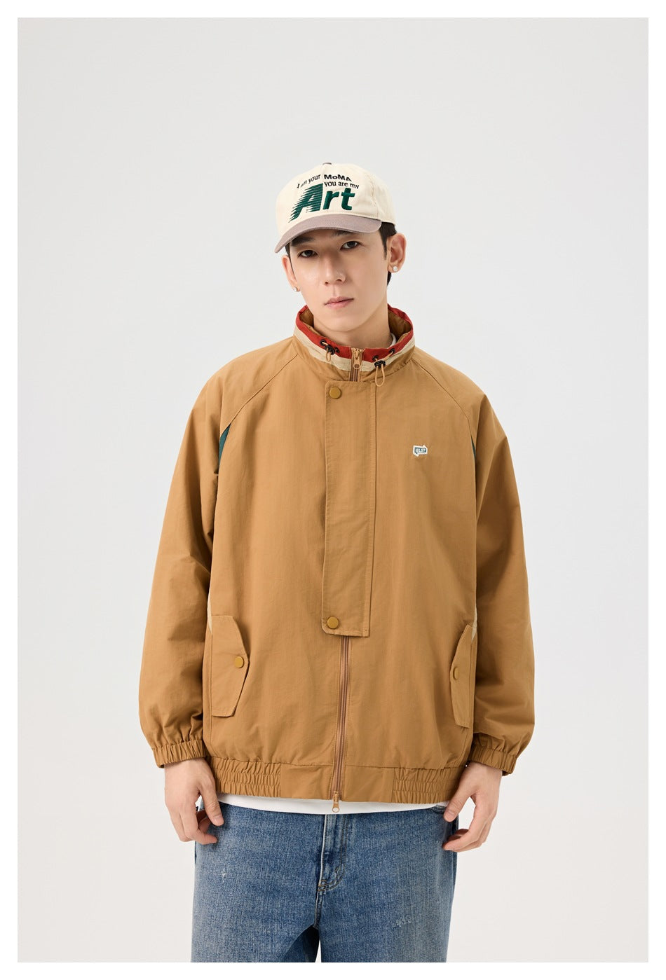 Front view of a model wearing a tan hooded jacket with dark teal side panels and elastic cuffs and hem.
