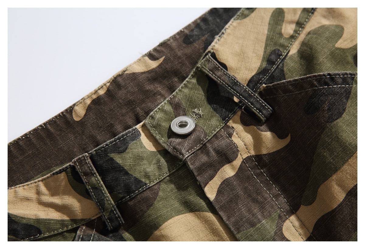Close-up of camouflage trousers showing the waistband, belt loops, and a metal snap closure.