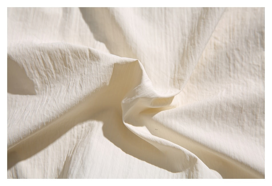 Close-up of softly crinkled ivory garment fabric, gathered into gentle folds.