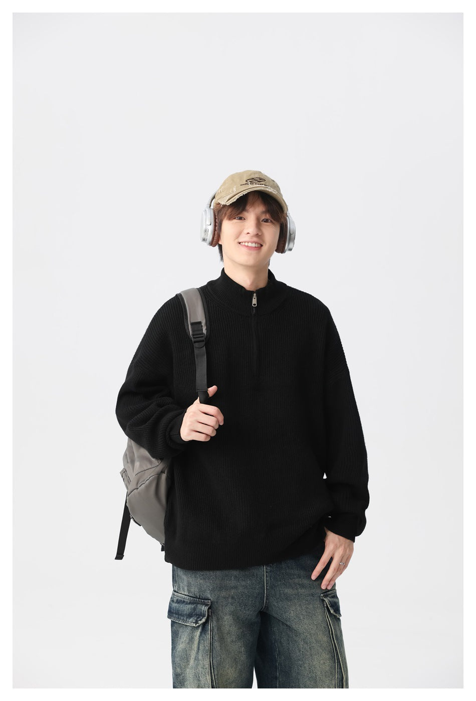 Model wearing a black ribbed quarter-zip sweater with a stand collar, backpack and headphones.