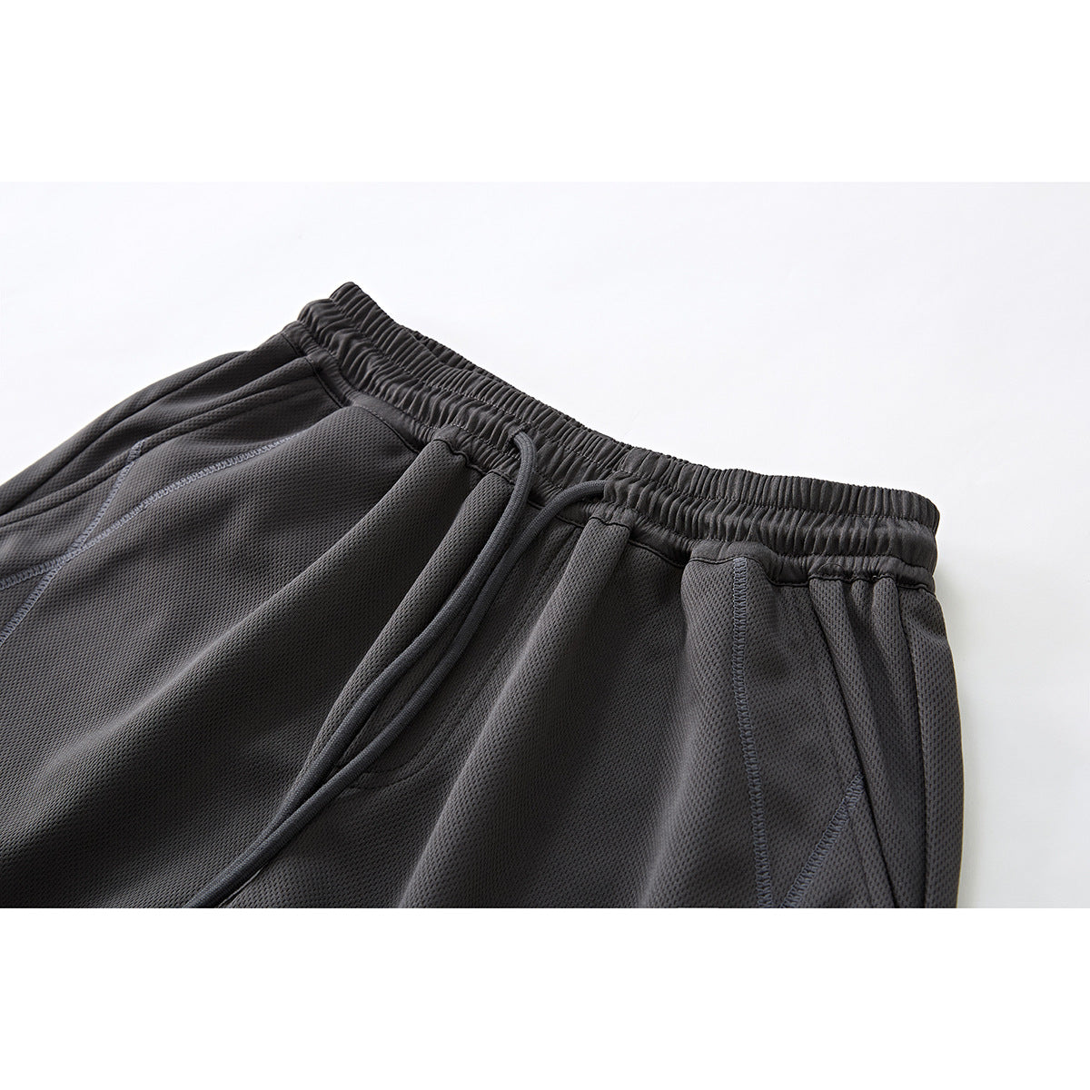 Close-up of charcoal shorts showing the elastic drawstring waistband, pocket opening and stitched panels.
