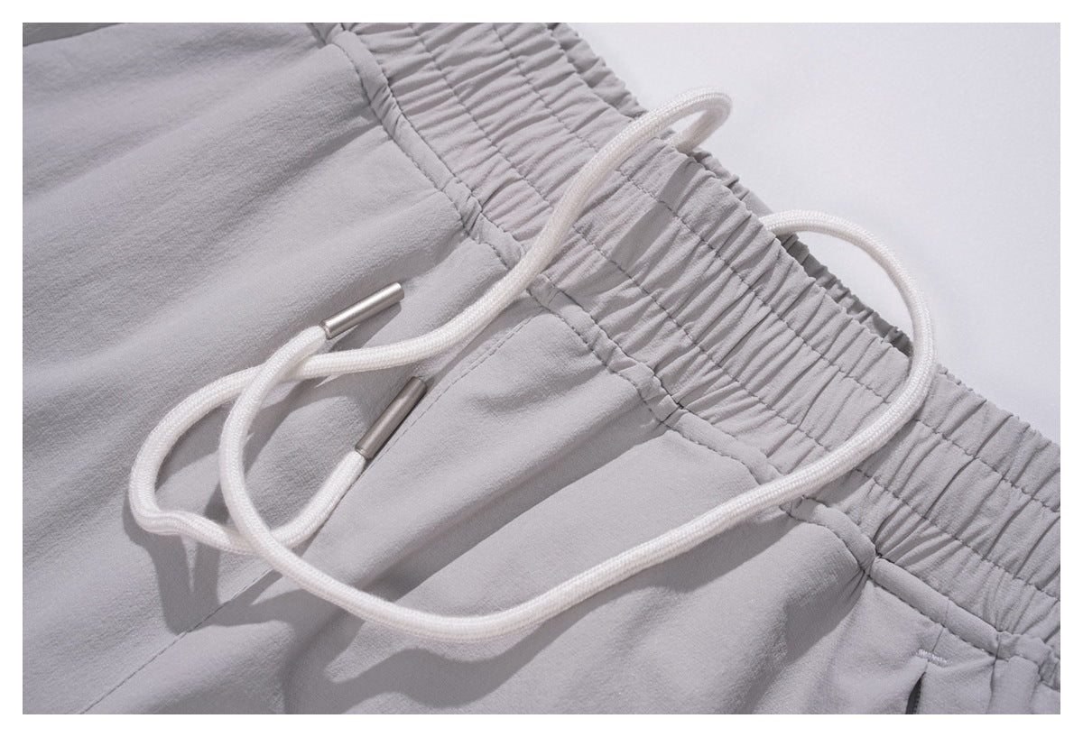 Close-up of light gray trousers with a gathered elastic waistband and white drawstring with metal tips.