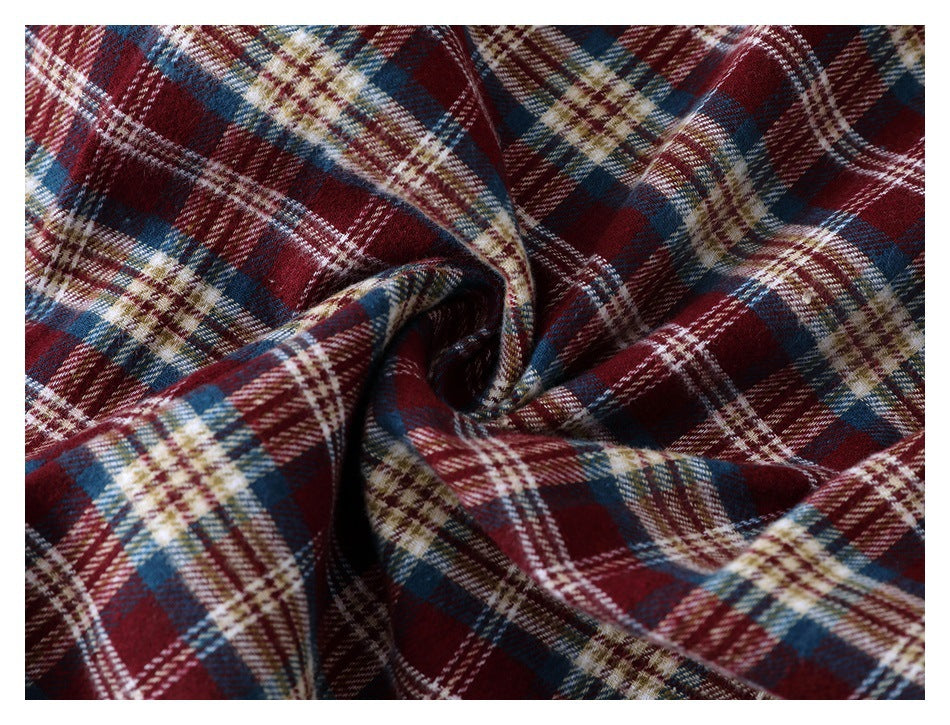 Close-up of burgundy, navy, cream, and tan plaid fabric gathered to show its texture and drape.