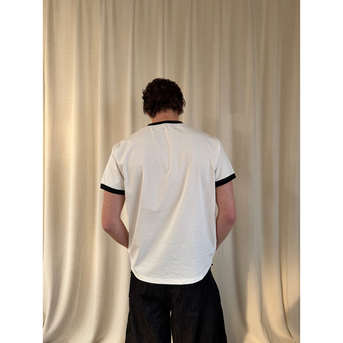Back view of a model wearing a white T-shirt with black collar and sleeve bands.
