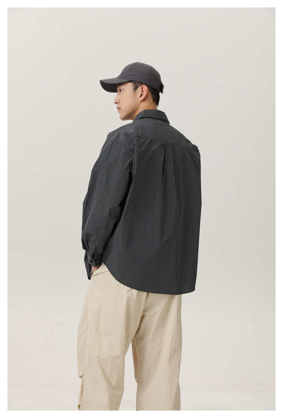 Back view of model wearing the black and white check shirt with a center pleat and buttoned cuff