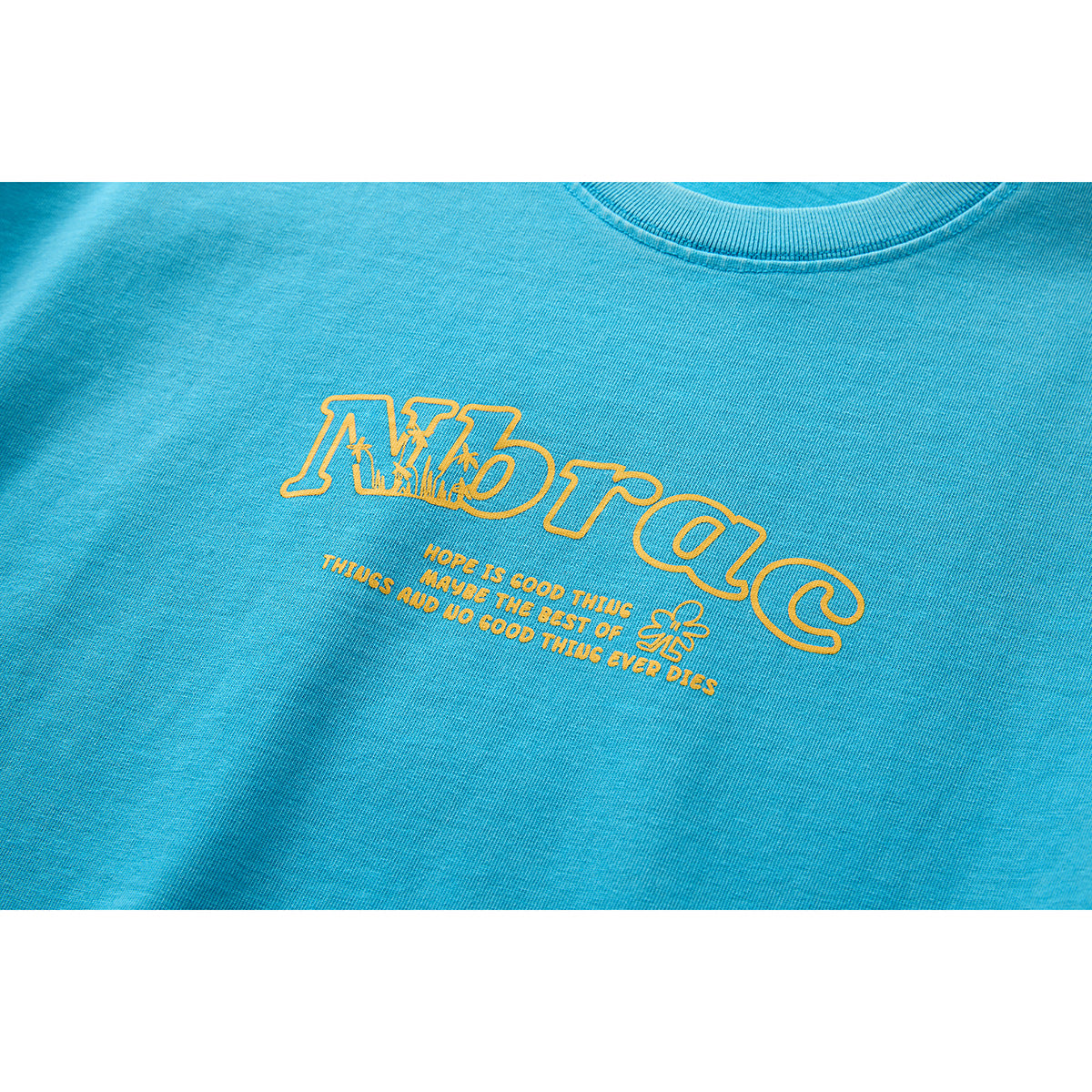 Close-up of a turquoise T-shirt with a yellow outlined wordmark and small text printed on the chest.