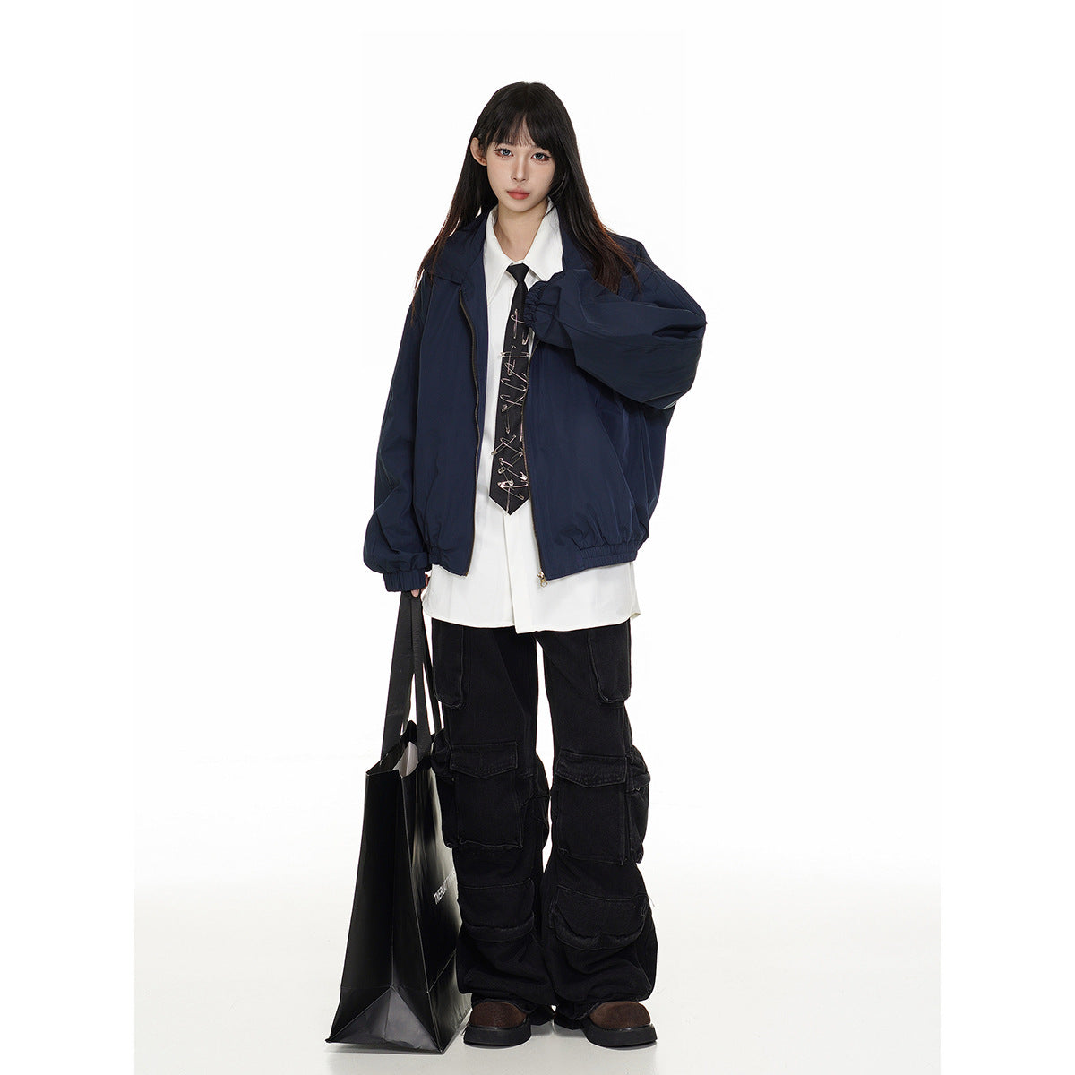 Model wearing an oversized navy zip jacket with elastic cuffs and hem, layered over a white shirt and tie.