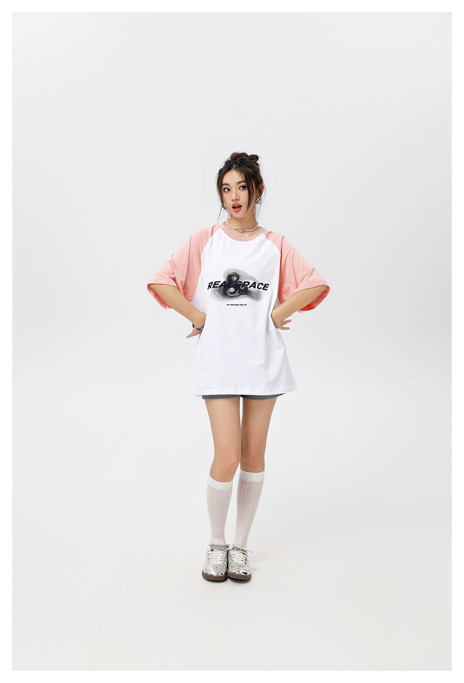 Model wearing a white oversized raglan T-shirt with pale pink sleeves and a black chest graphic, standing with hands on hips.