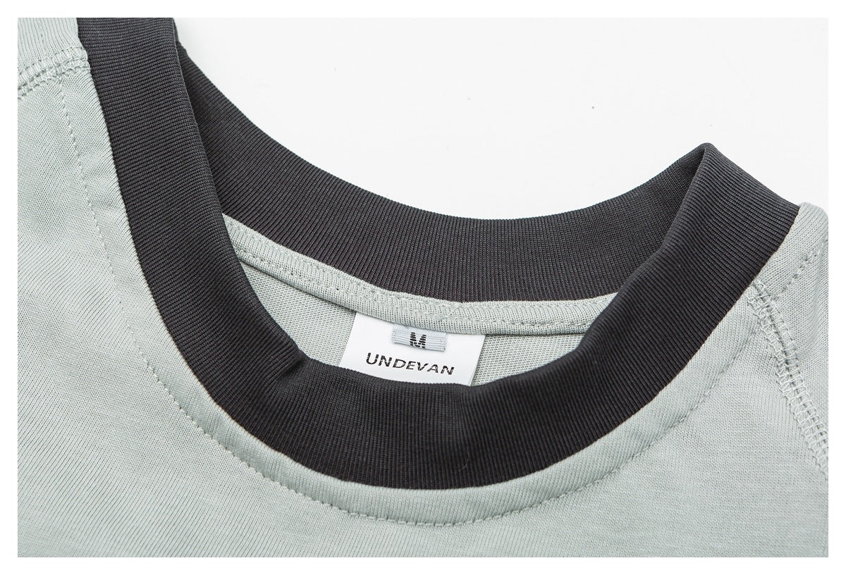 Close-up of a pale sage shirt with a dark ribbed crew neck and a visible UNDEVAN neck label.