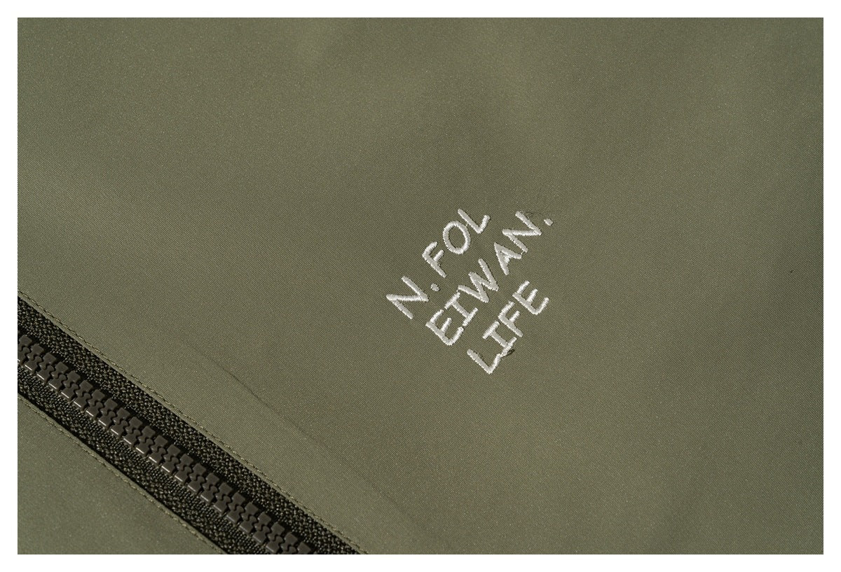 White embroidered lettering beside the zipper on olive jacket fabric.