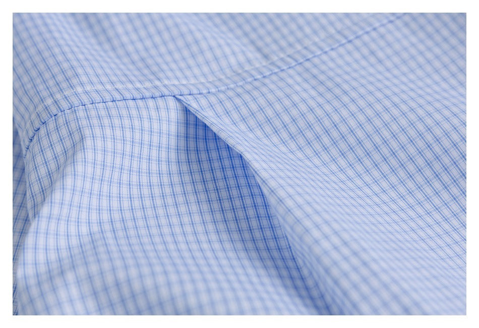 Close-up of stitching and overlapping seams on light blue checked shirt fabric.