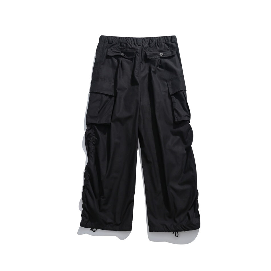 Back view of black cargo pants with button-flap rear pockets, large side pockets, and gathered drawcord hems.