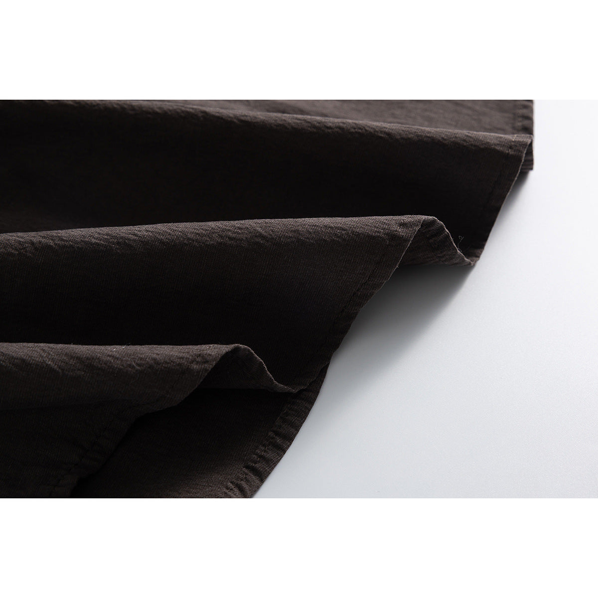 Close-up of dark brown shirt fabric folded to show its surface and stitched edge.