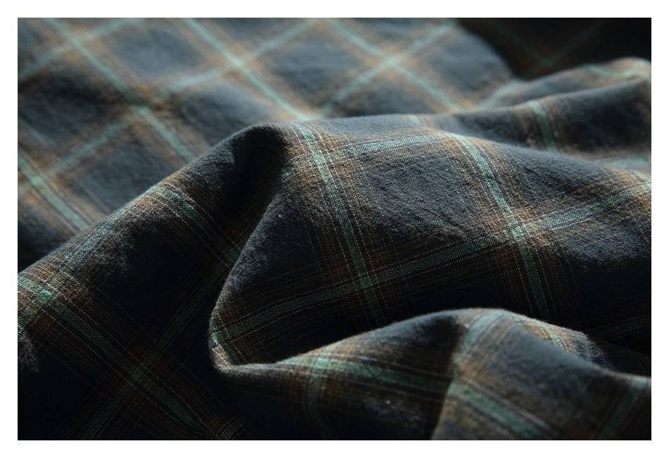 Close-up of dark plaid fabric with muted green and tan lines draped in soft folds.