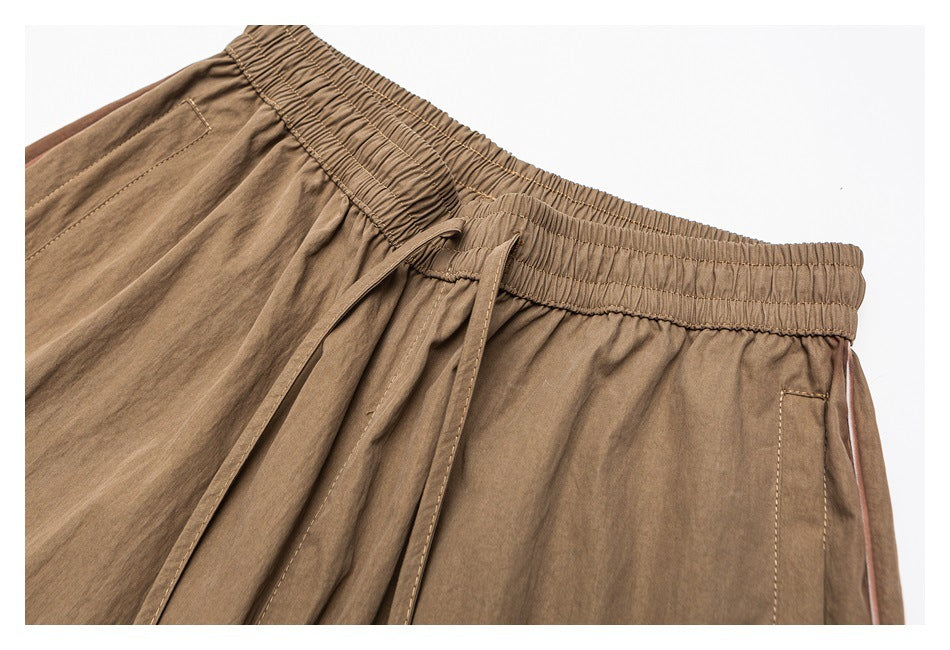 Close-up of tan pants showing the elastic waistband, front drawstring, and side pocket.