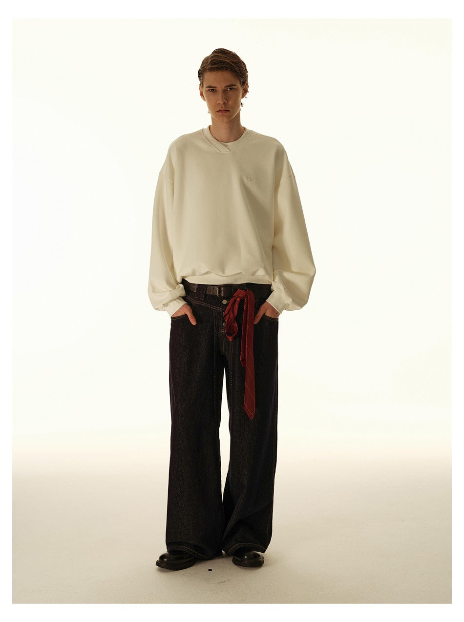 Model wearing an oversized cream sweatshirt with wide-leg dark jeans and a red scarf tied at the waist.