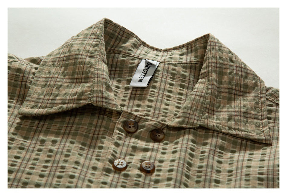 Flat-lay close-up of an olive and tan plaid shirt collar with brown buttons and a sewn neck label.