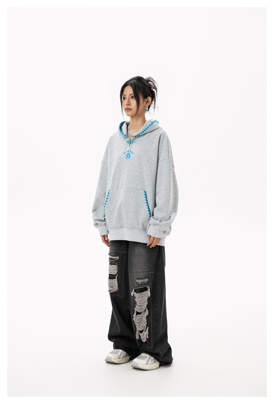 Model wearing an oversized heather gray hoodie with blue trim and wide-leg ripped black jeans, side view