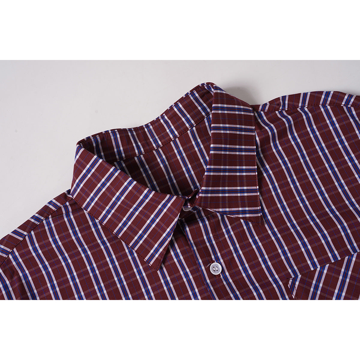 Close-up of a burgundy plaid button-up shirt collar and upper chest with a white button.