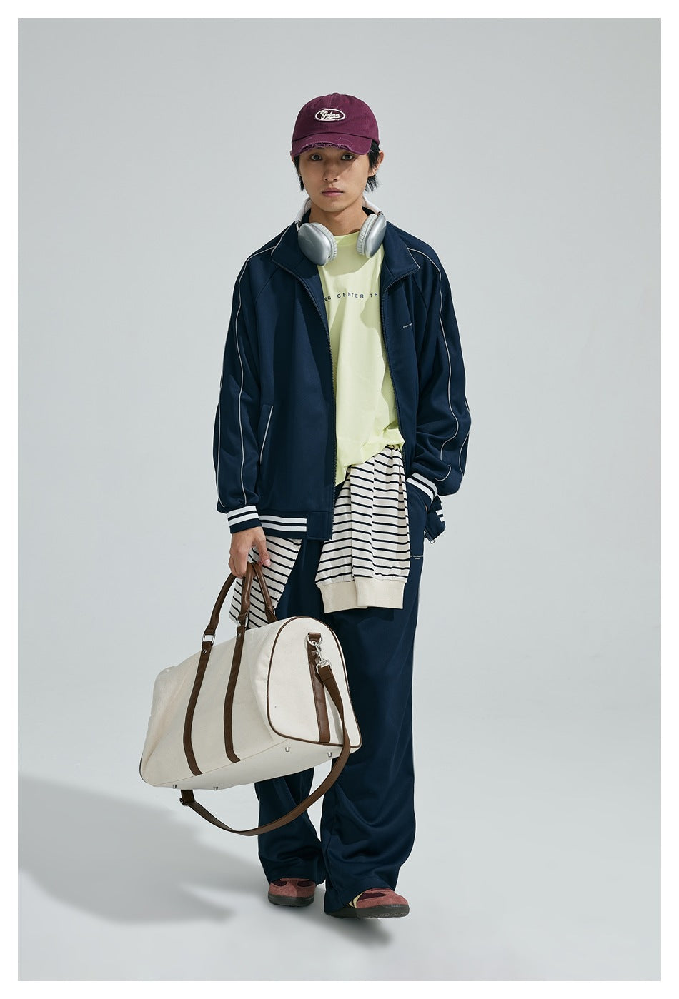 Full-length front view of a model wearing a navy tracksuit with white piping, pale yellow and striped layers, and a white