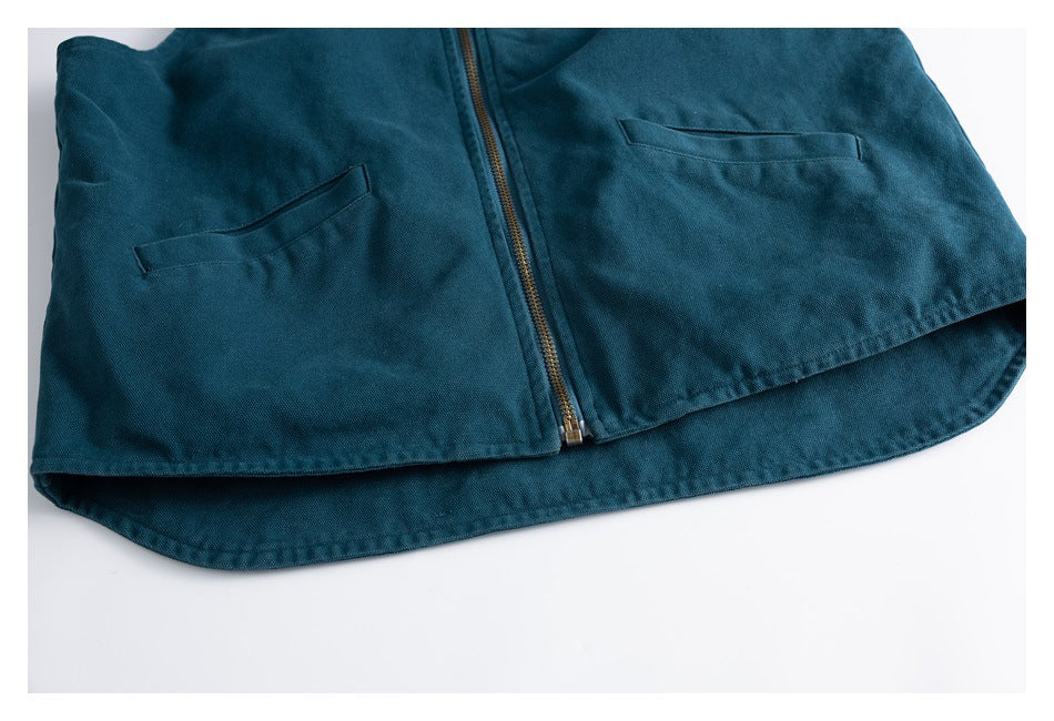 Cropped front view of a teal zip-front garment with two pockets and a rounded hem, laid flat.