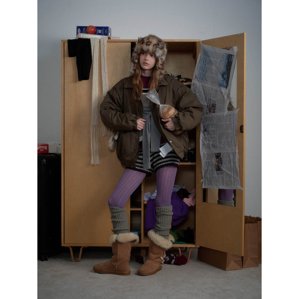 Full-length model wearing an oversized olive jacket, spotted fur hat, purple tights, gray leg warmers and brown boots.