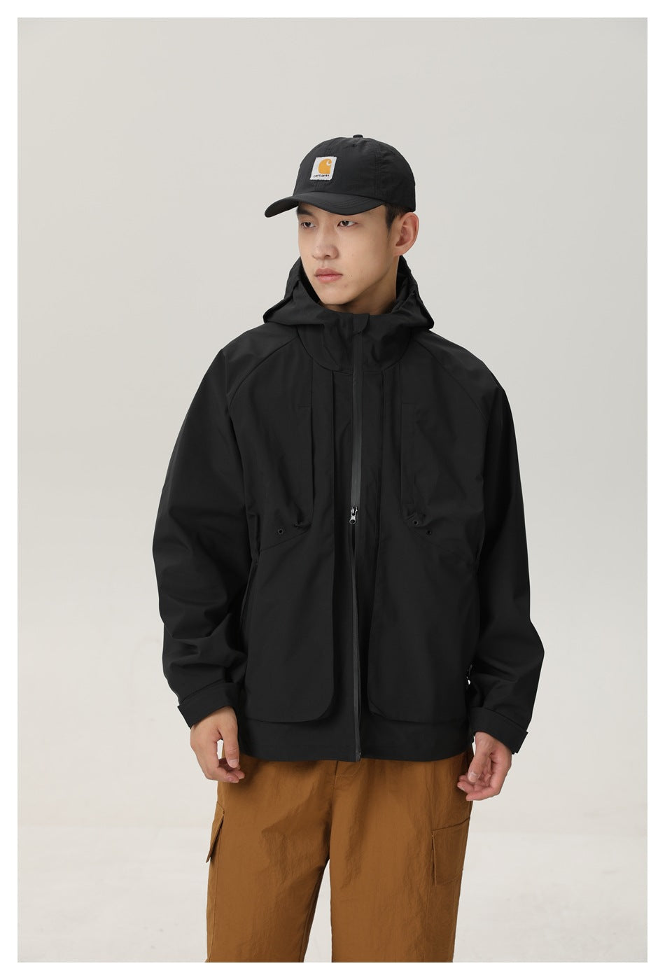 Front view of a model wearing a black hooded jacket with a zip front and flap pockets, framed by a white border.
