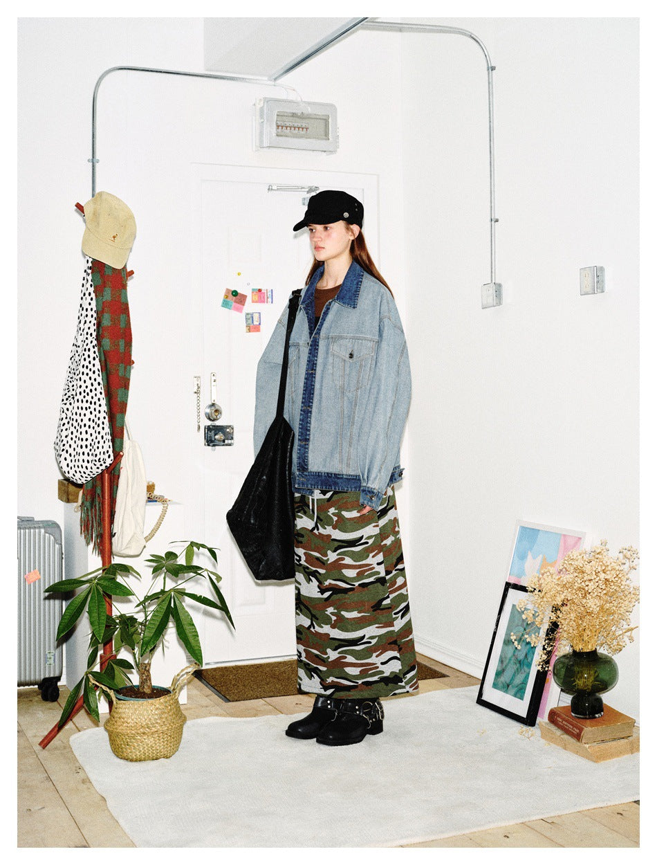 Model wearing an oversized light blue denim jacket with dark denim trim and a camouflage maxi skirt.