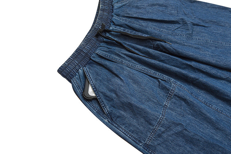 Close-up of blue denim trousers showing the elastic waistband, black drawstring, and a side pocket with a phone tucked