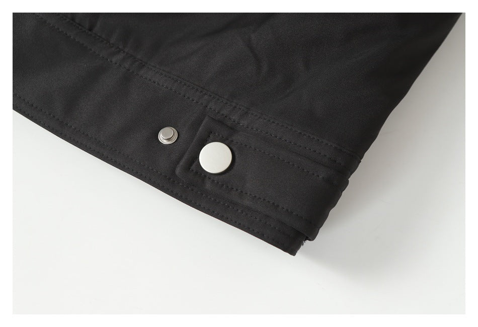 Close-up of a black jacket hem with stitched seams and a silver snap fastener.