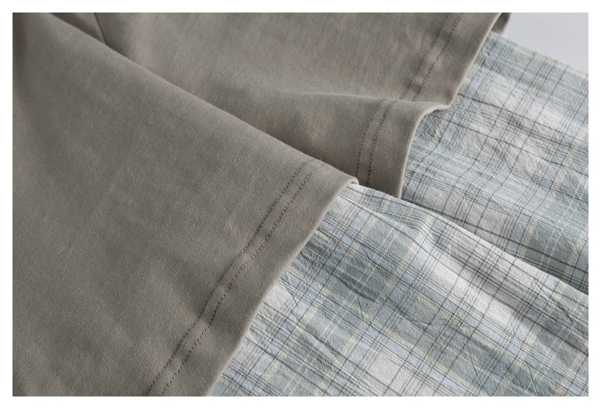 Close-up of taupe T-shirt fabric and hem over pale blue-gray plaid fabric.